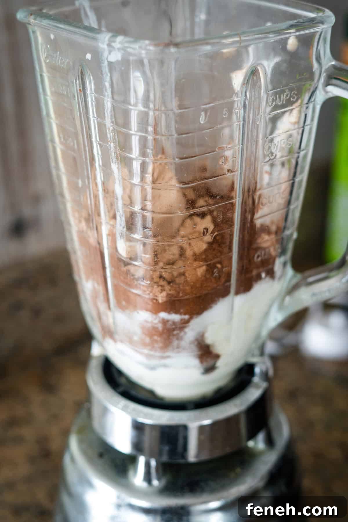 A blender containing cocoa powder, yogurt, and other ingredients is placed on a countertop, ready to blend.