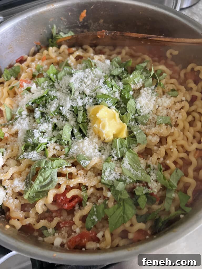 Butter, fresh basil and parmesan cheese just added to pasta in pan.