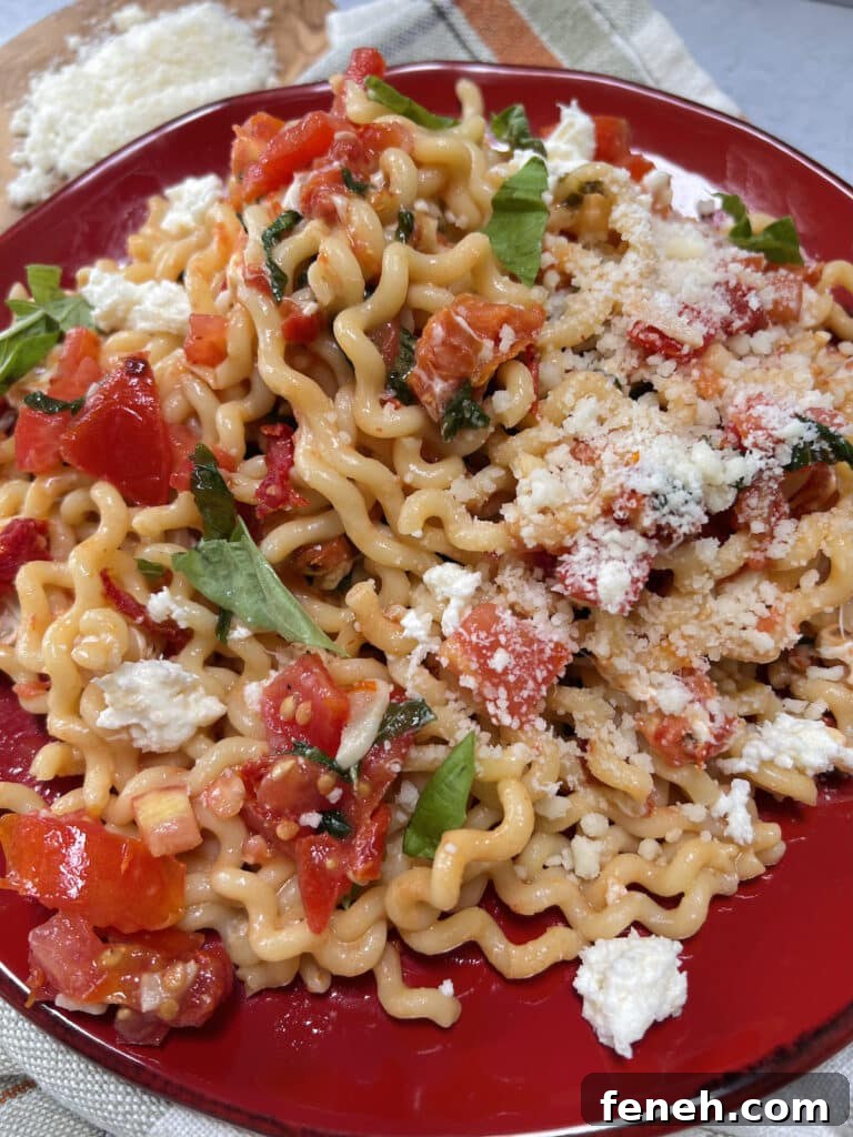 Overhead view of fusilli with tomato, basil and fresh mozzarella on red plate.