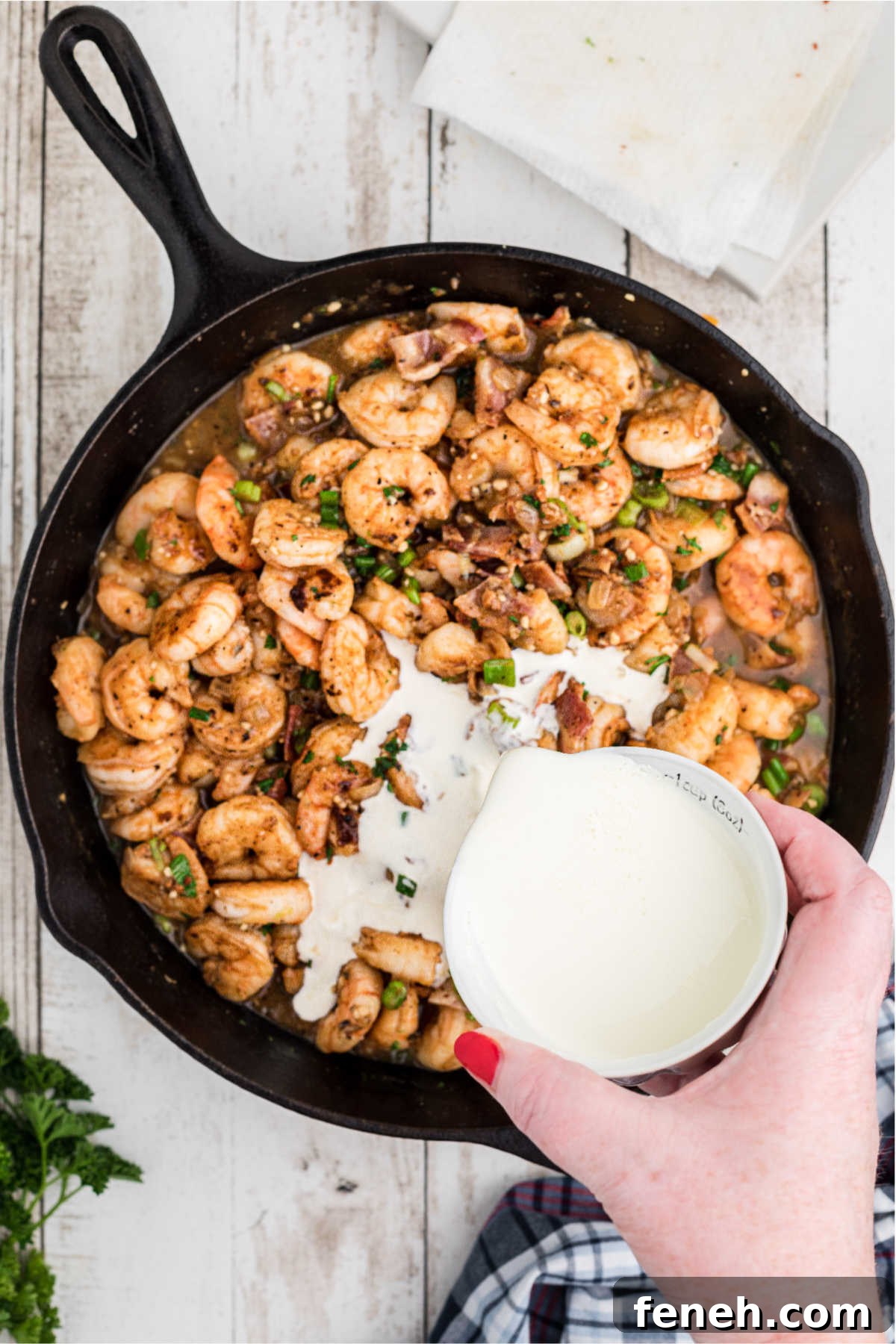 Cream being poured into a cast iron skillet with shrimp and bacon.