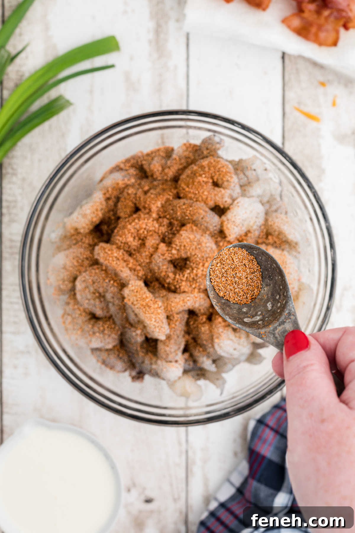 A large mixing bowl with some seasoning being sprinkled over shrimp.