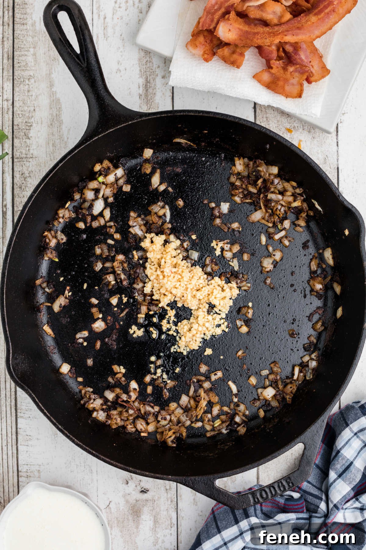 Garlic being added to some onions in a cast iron skillet.