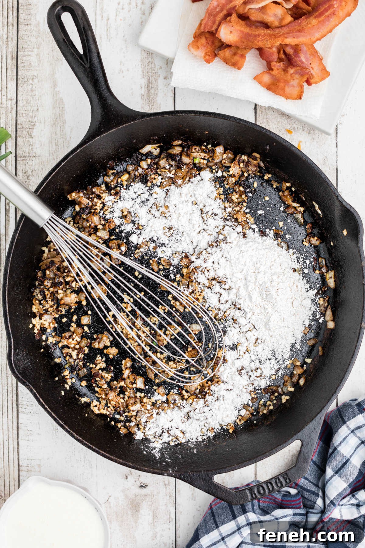 Flour being added to a cast iron skillet with onions and garlic.