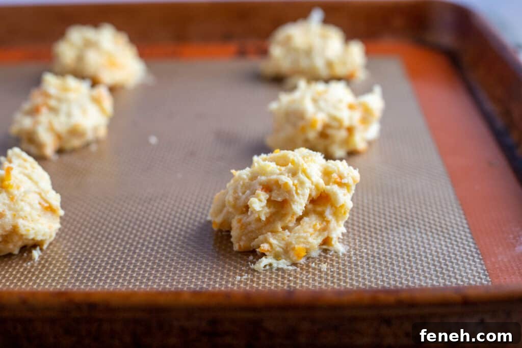 A baking sheet with a silicone baking mat sits with six unbaked carrot cookies ready to go into the oven.