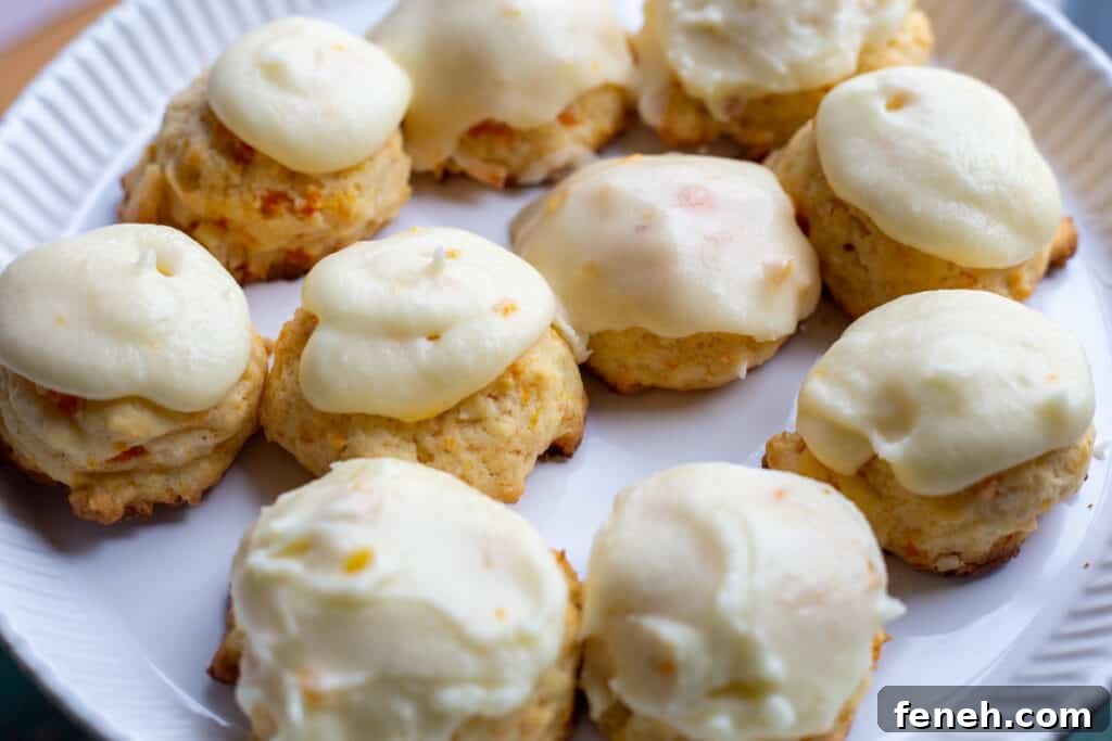 Ten carrot cookies with orange icing sit on a white plate.