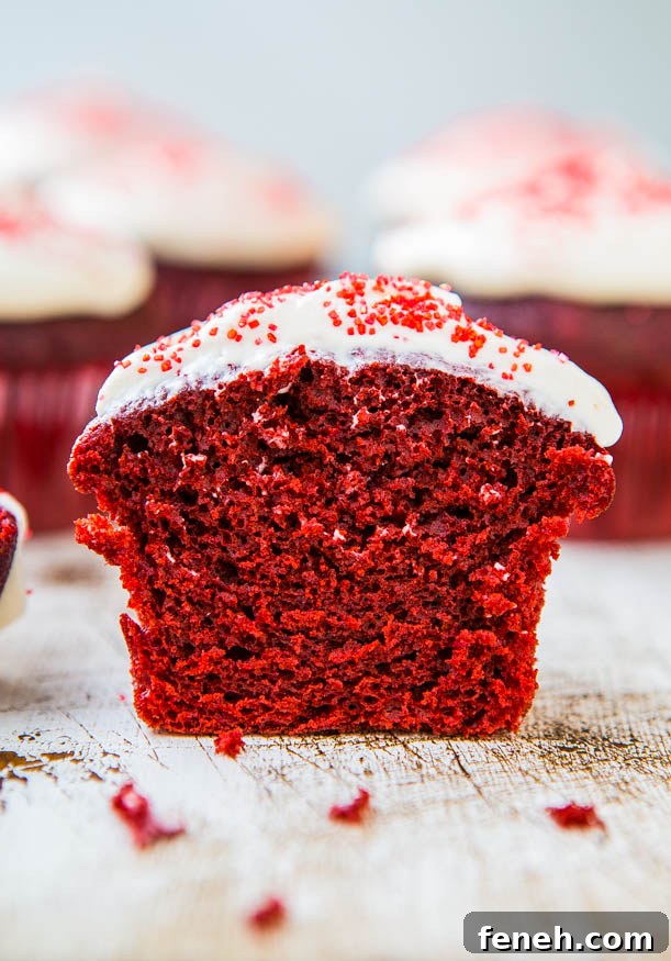 Red Velvet Cupcakes with Silky Vanilla Cream Cheese Frosting 3 A red velvet cupcake with cream cheese frosting and red sprinkles, partially eaten.