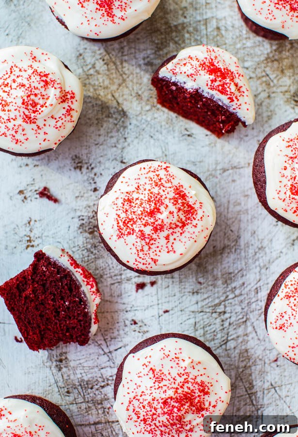 Red Velvet Cupcakes with Silky Vanilla Cream Cheese Frosting 4 Red velvet cupcakes with cream cheese frosting and red sprinkles, one partially eaten.