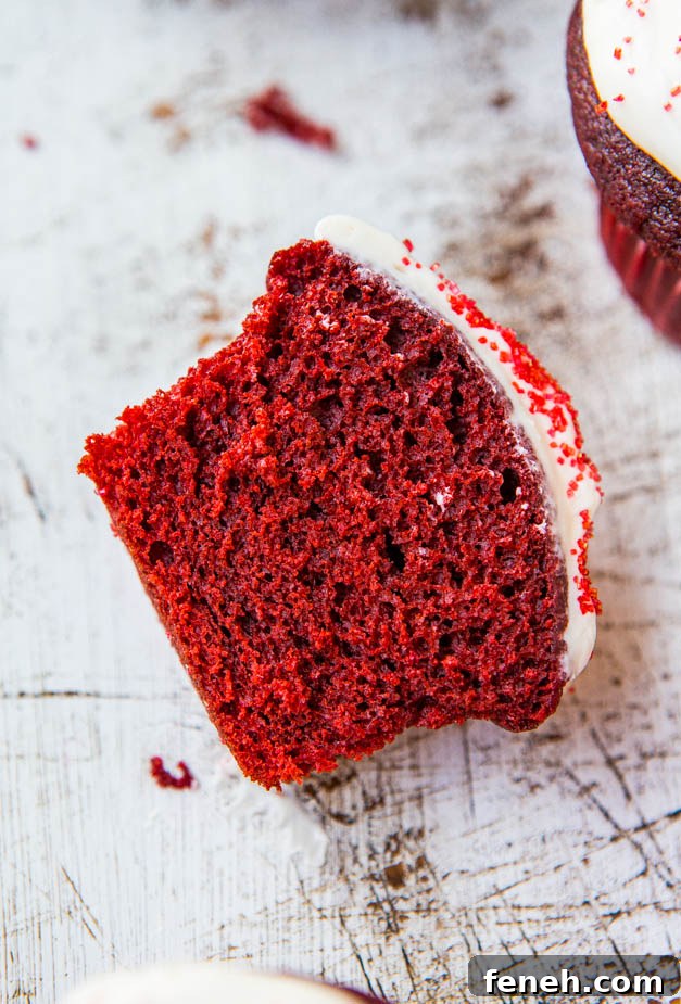 Red Velvet Cupcakes with Silky Vanilla Cream Cheese Frosting 5 A close-up of a bitten red velvet cupcake with cream cheese frosting on a white rustic background.