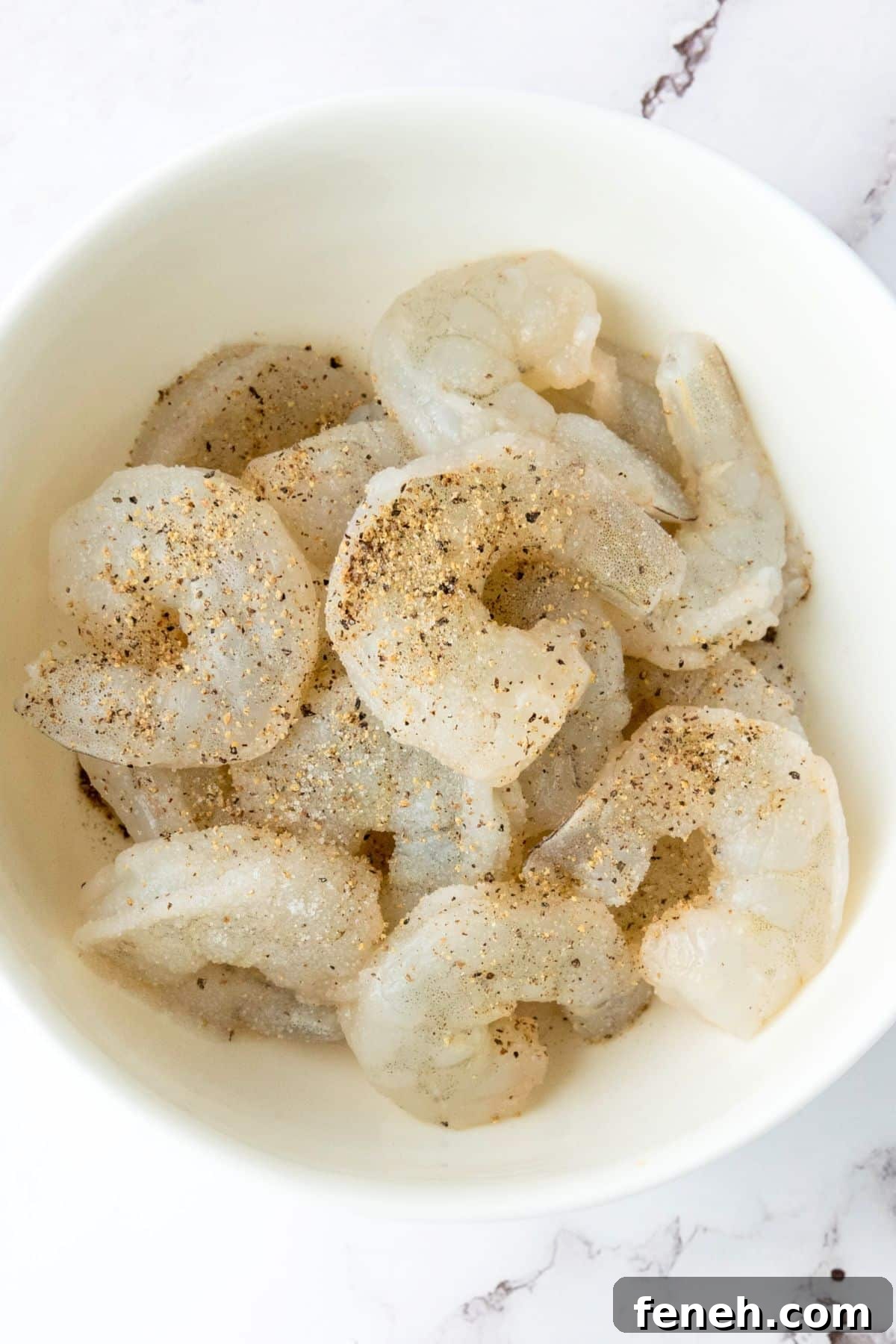 Top down view of bowl of raw shrimp seasoned with salt and pepper.