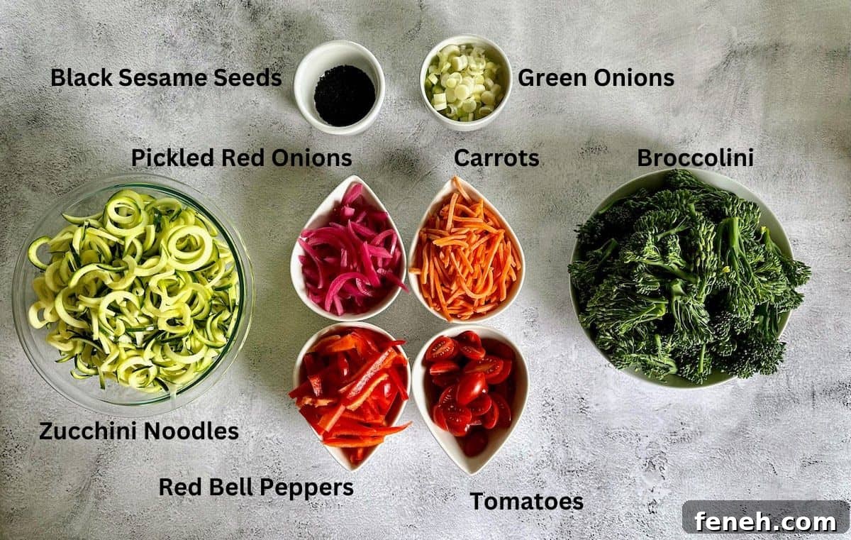 Salad ingredients: zucchini noodles, pickled red onions, carrots, tomatoes, red bell peppers, broccolini, black sesame seeds, and green onions. 