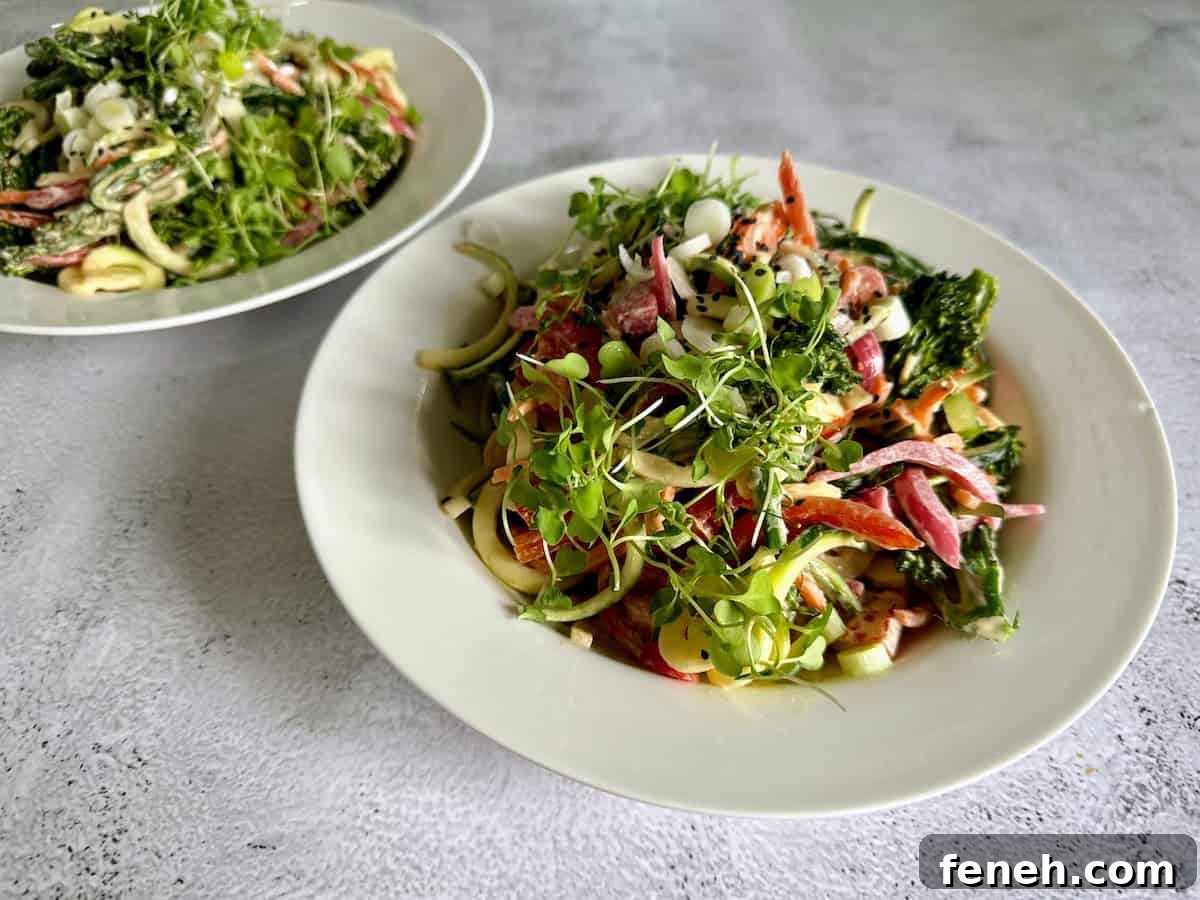 Zucchini Noodle Salad in two bowls on the table garnished with green onions, black sesame seeds, and microgreens. 