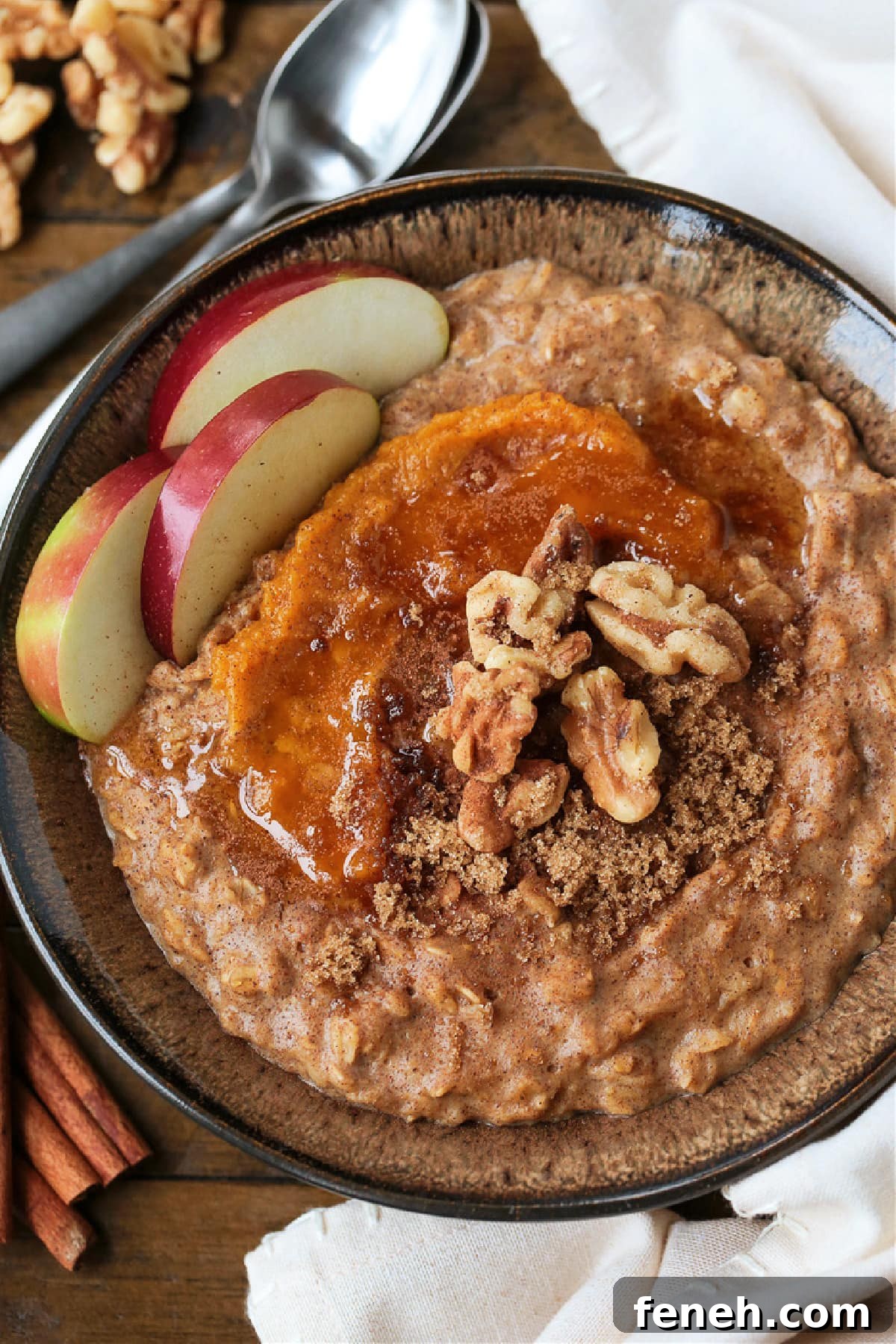 A bowlful of pumpkin oatmeal topped with apples, walnuts and pumpkin puree, with a spoon.