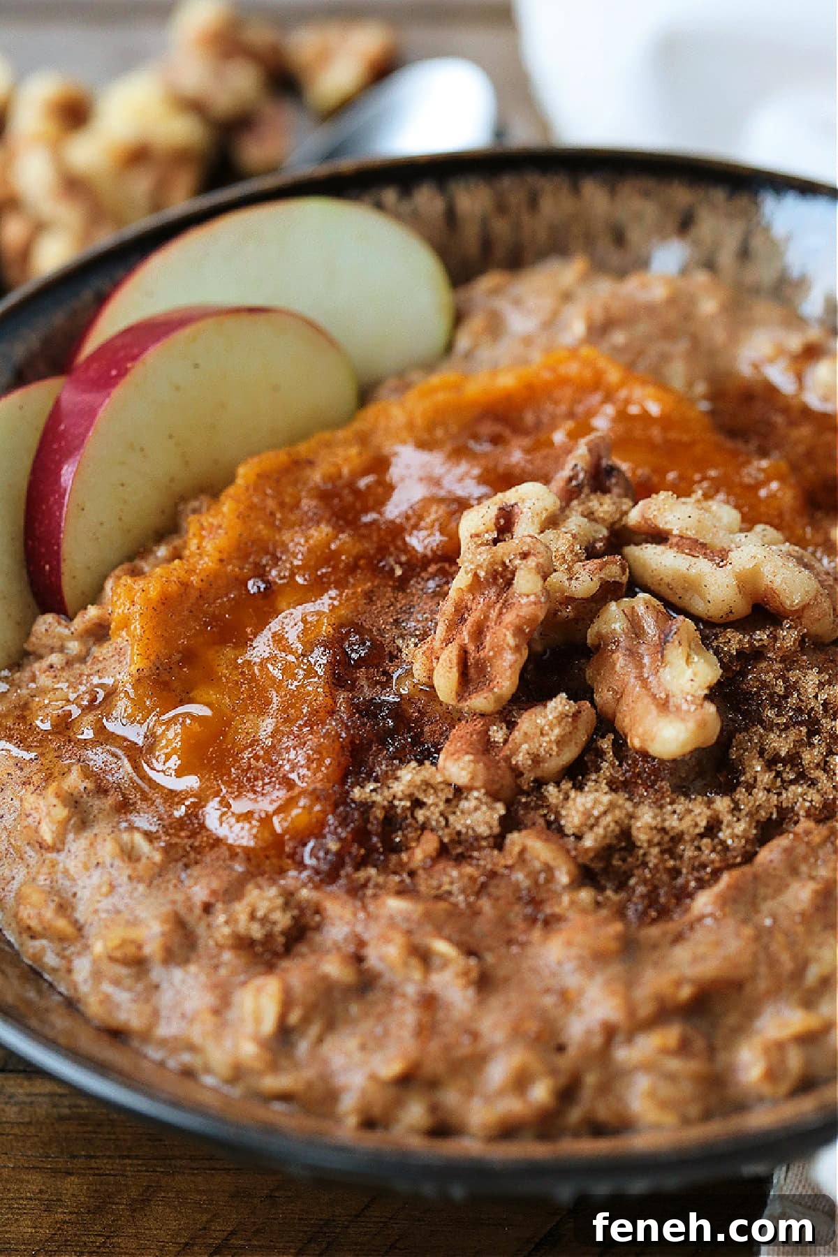 A bowlful of pumpkin oatmeal topped with apples, walnuts and pumpkin puree, with a spoon.