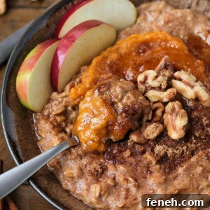 A bowlful of pumpkin oatmeal topped with apples, walnuts and pumpkin puree, with a spoon.