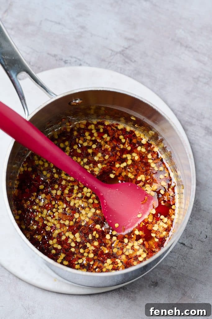 simmering honey with chili flakes in a saucepan with a red spatula