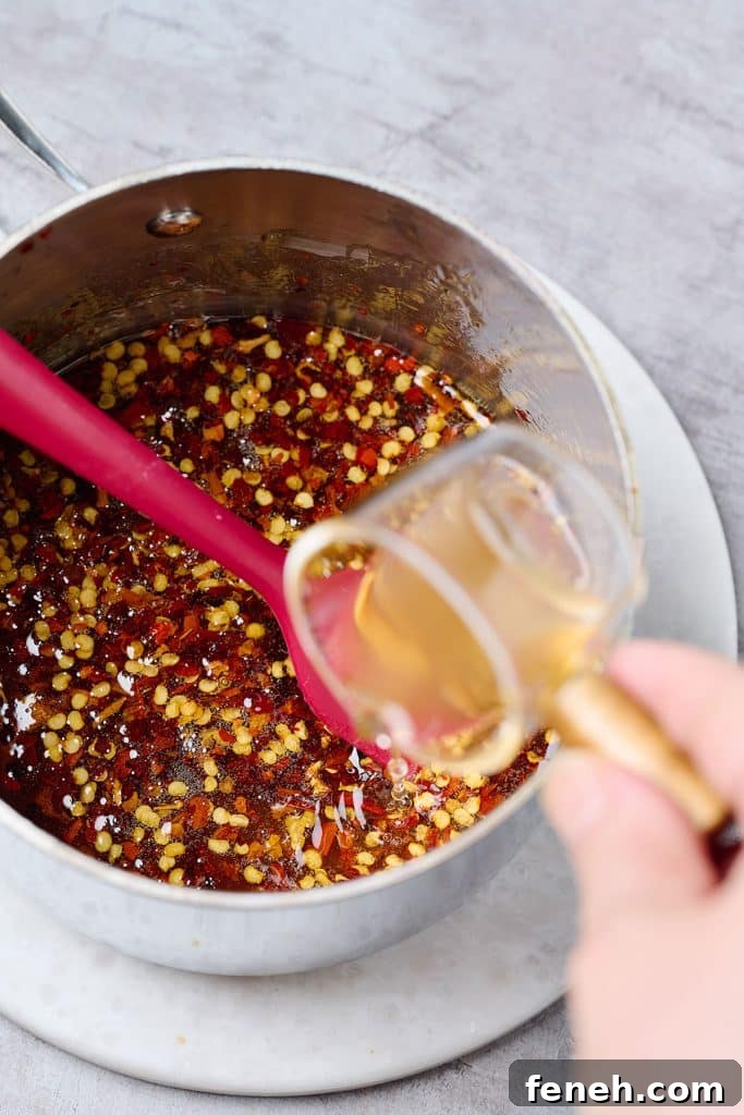 pouring apple cider vinegar into the hot honey sauce