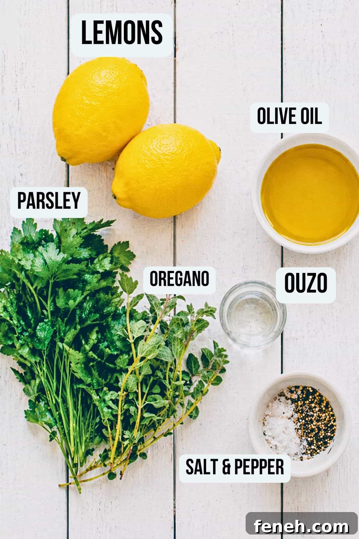 Ingredients for Greek salad dressing including lemons, olive oil, parsley, oregano and ouzo on a white surface.