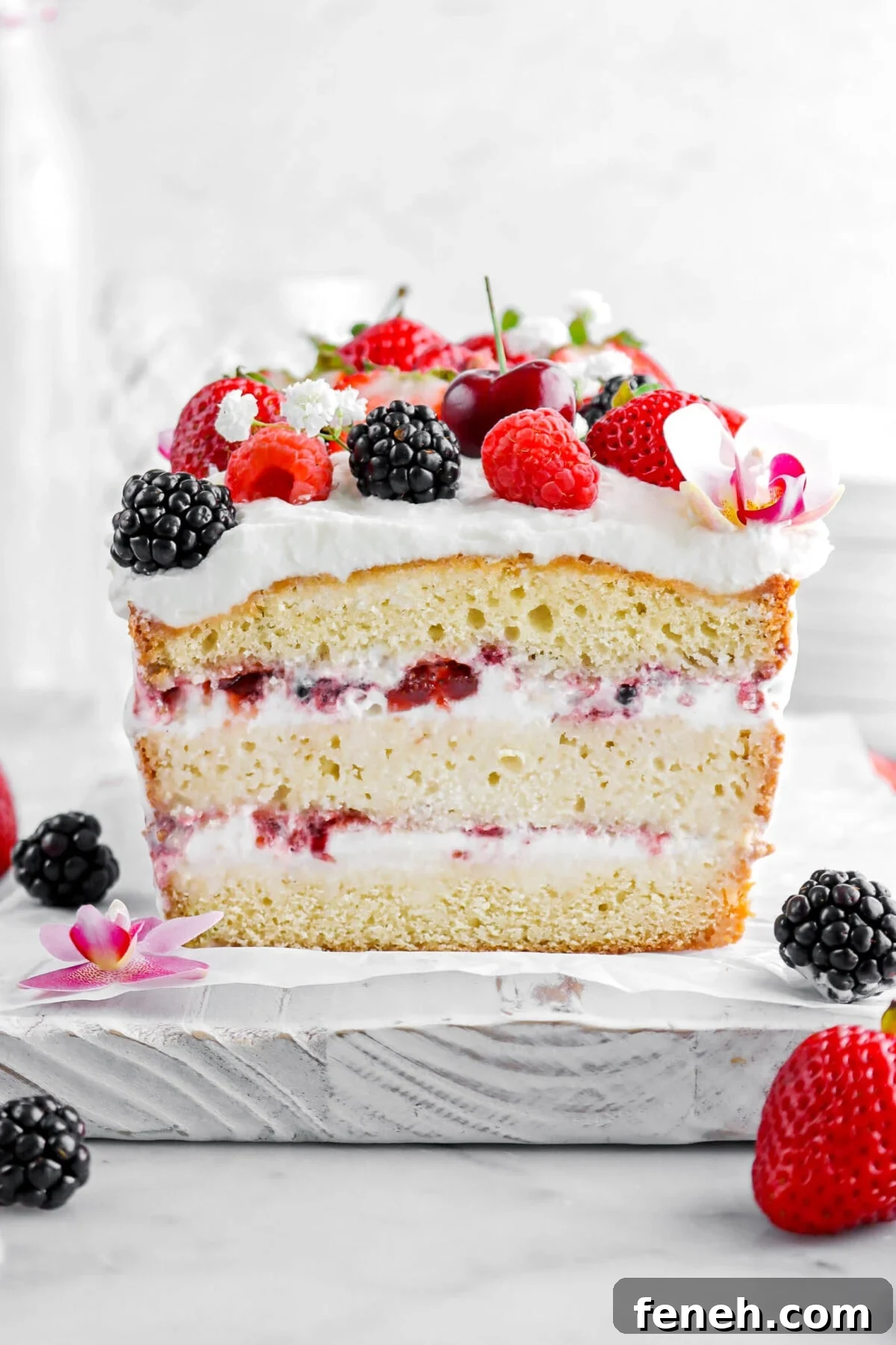 close up of ice cream loaf cake on white board with berries and whipped cream on top.