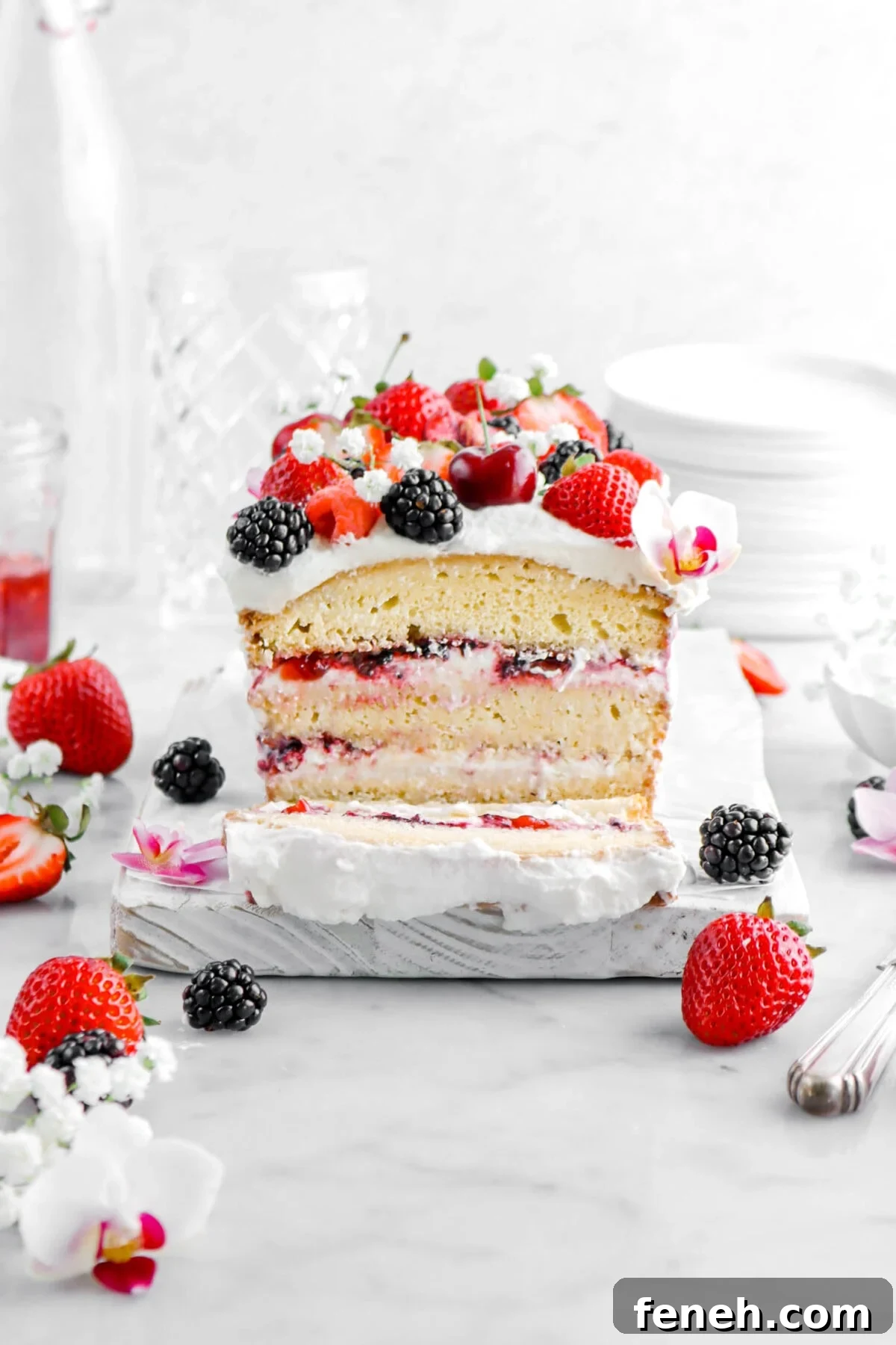 ice cream loaf cake with slice laying in front, with berries and flowers around on marble surface.