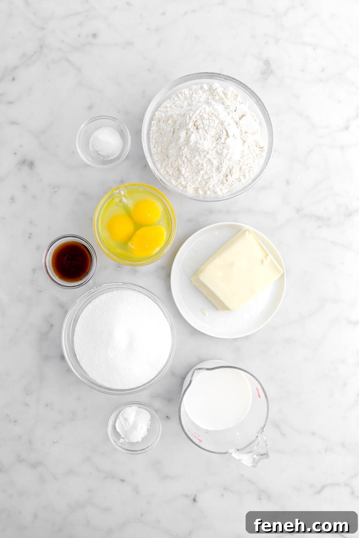salt, flour, eggs, butter, vanilla, sugar, milk, and baking powder on marble surface.