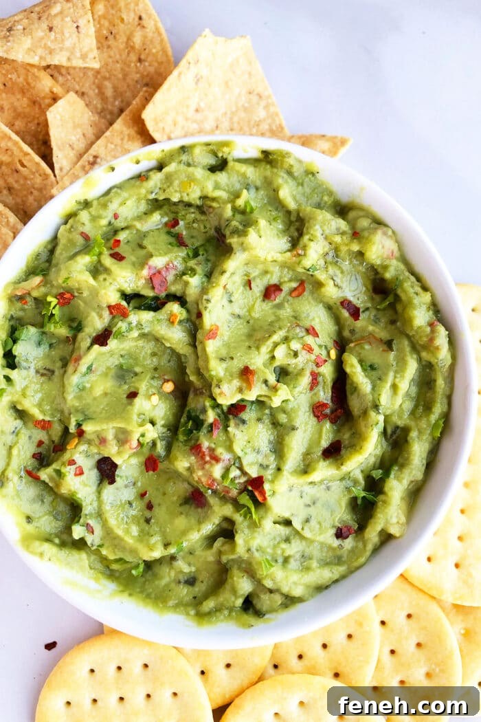 Spicy Mexican avocado dip in white bowl on large dish with crackers and tortillas. 
