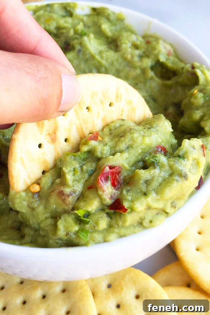 Cracker being dipped in bowl of green dip. 