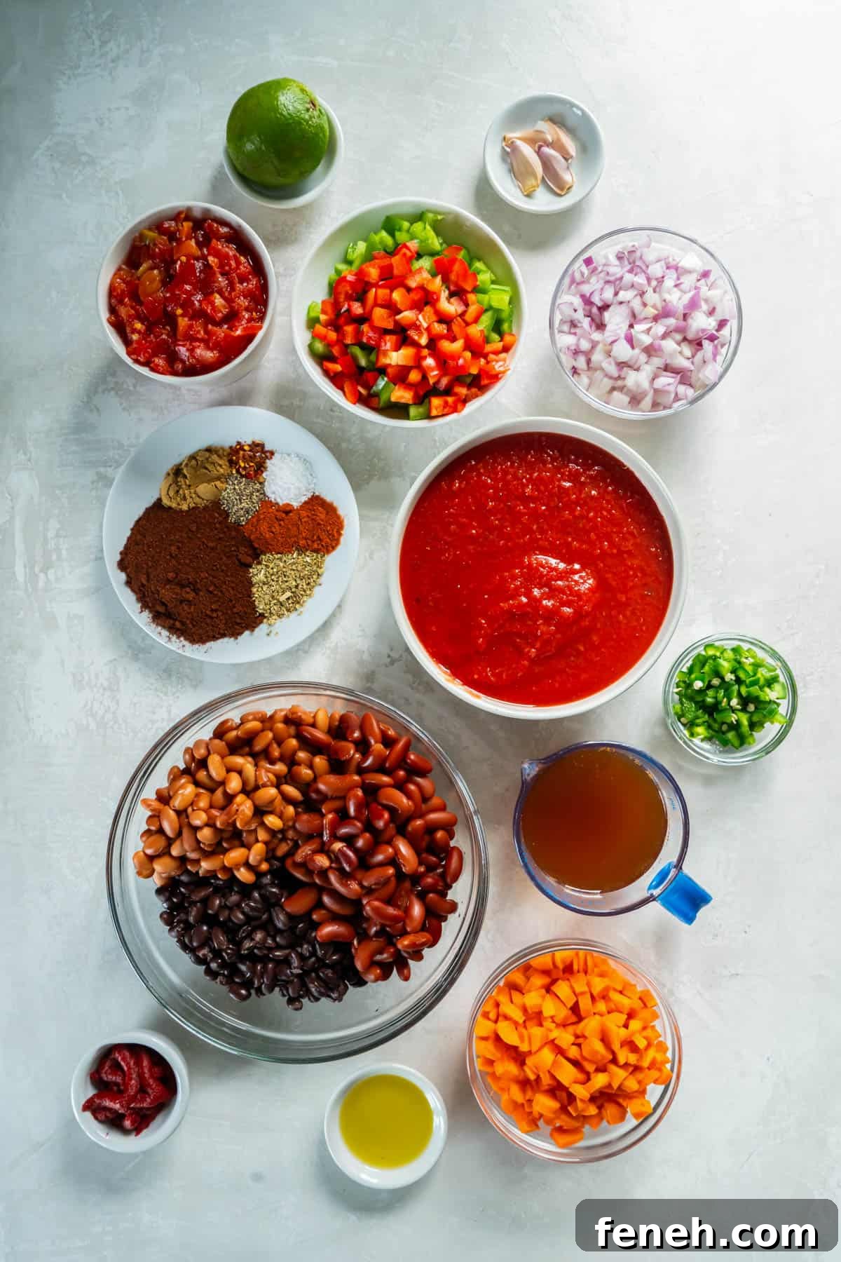 All of the ingredients for three bean chili in bowls on a white counter. 