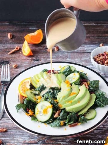 Orange Tahini Dressing being poured onto a lacinato kale salad.