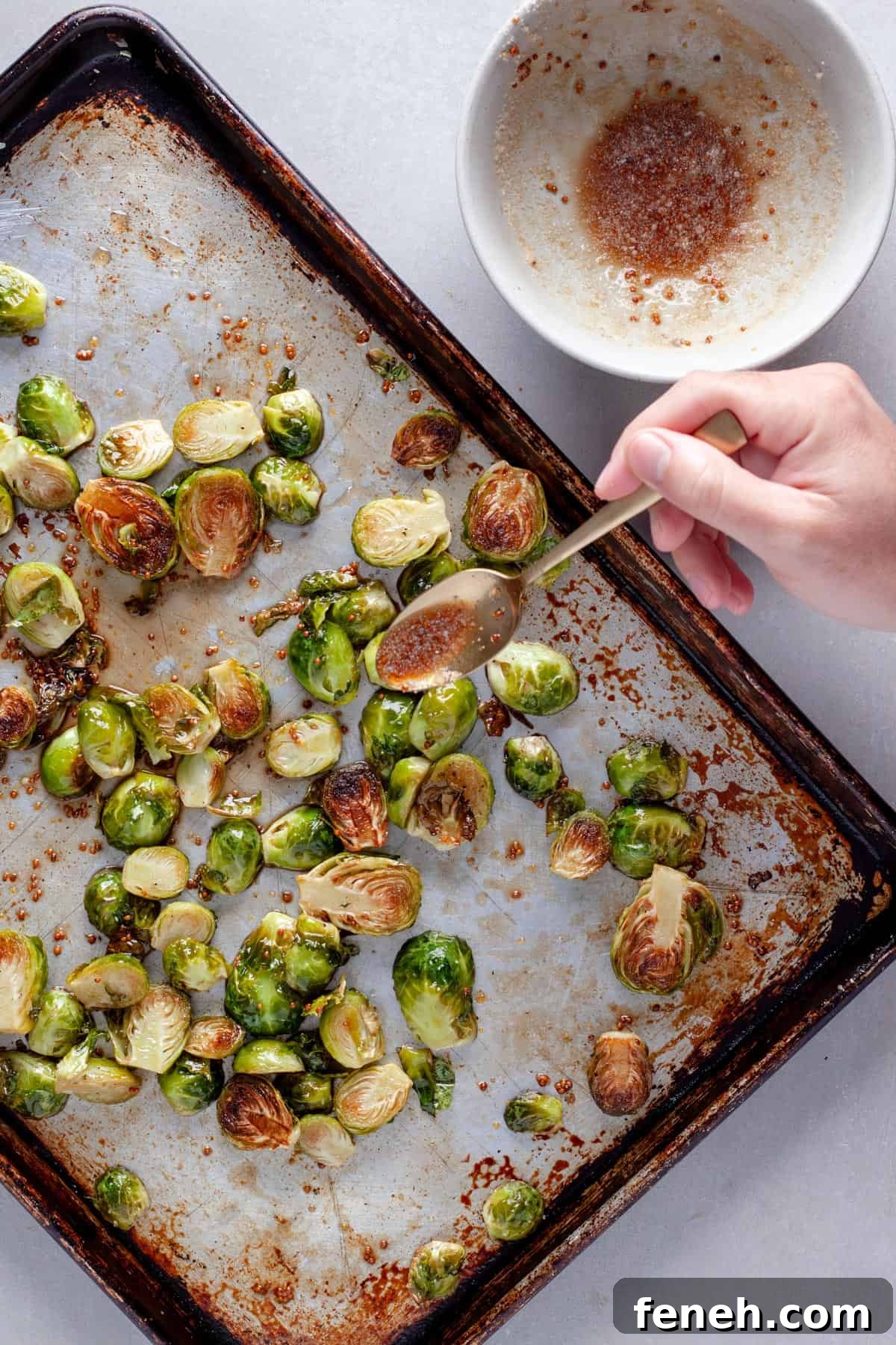 Roasted brussels sprouts get drizzled with maple balsamic vinegar sauce on a baking sheet.