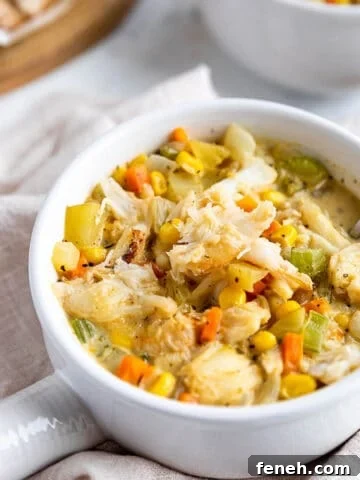 A soup bowl with a handle filled with a crab and corn chowder.