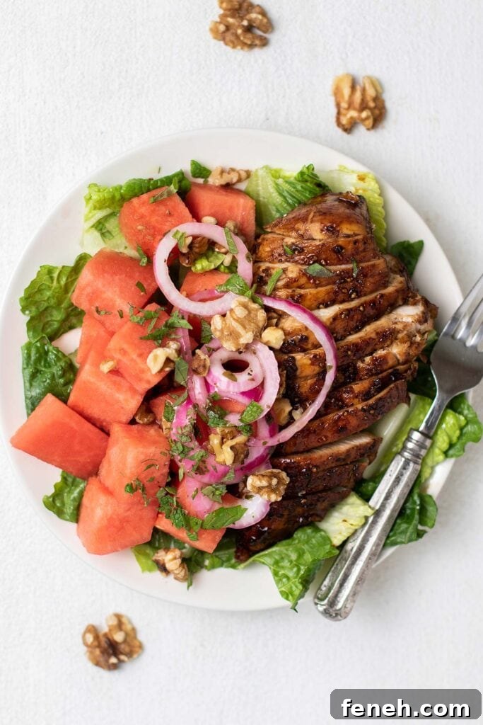 A white plate with lettuce, watermelon, and balsamic chicken.