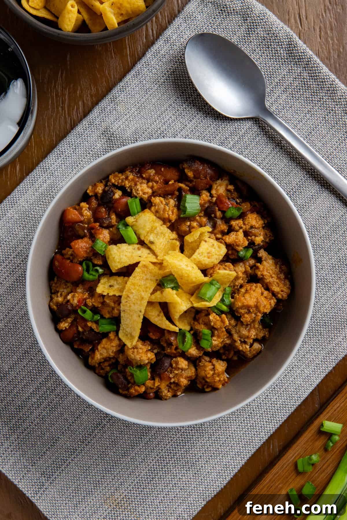 Overhead view of cooked chicken chili in a bowl topped with corn chips and sliced green onions.