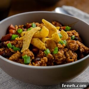 Cooked chicken chili topped with sliced green onions and corn chips.