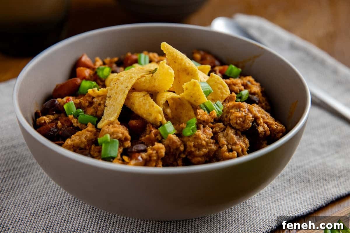 Overhead view of cooked chicken chili in a bowl topped with corn chips and sliced green onions.