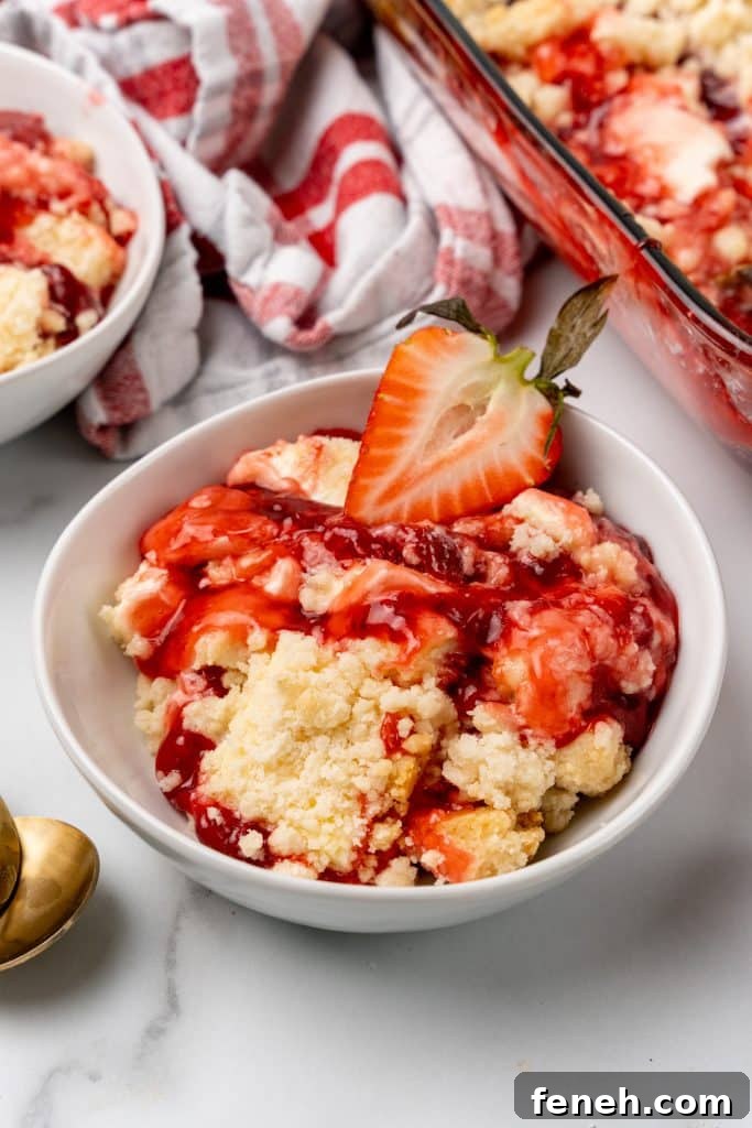strawberry cheesecake dump cake served in a white bowl with a fresh strawberry on top