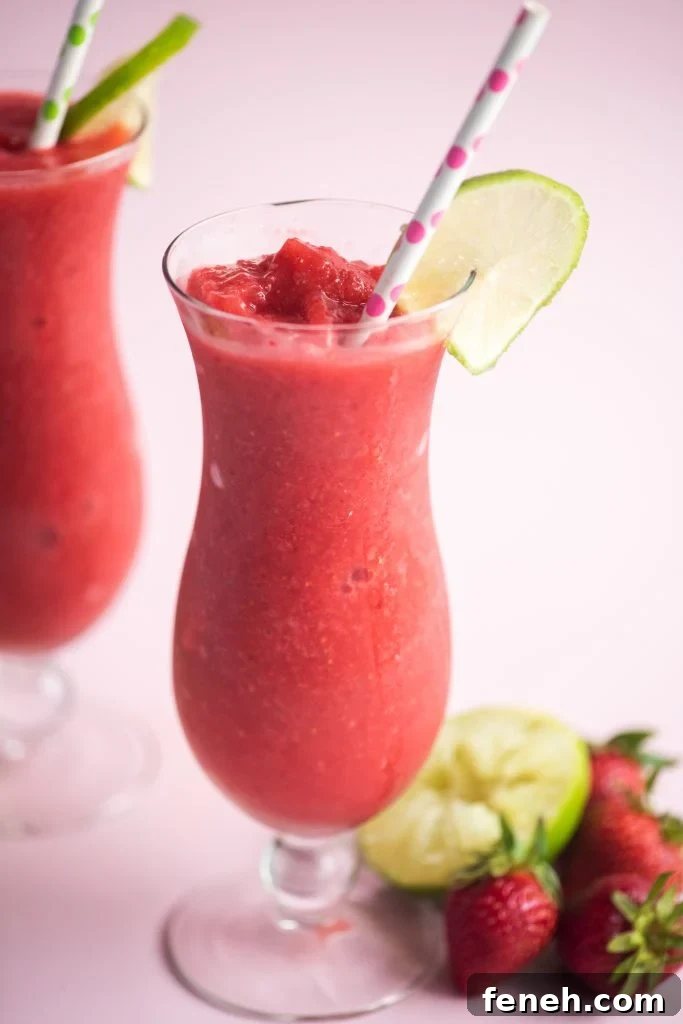 two strawberry daiquiris in glass jars garnished with lime slices and paper straws