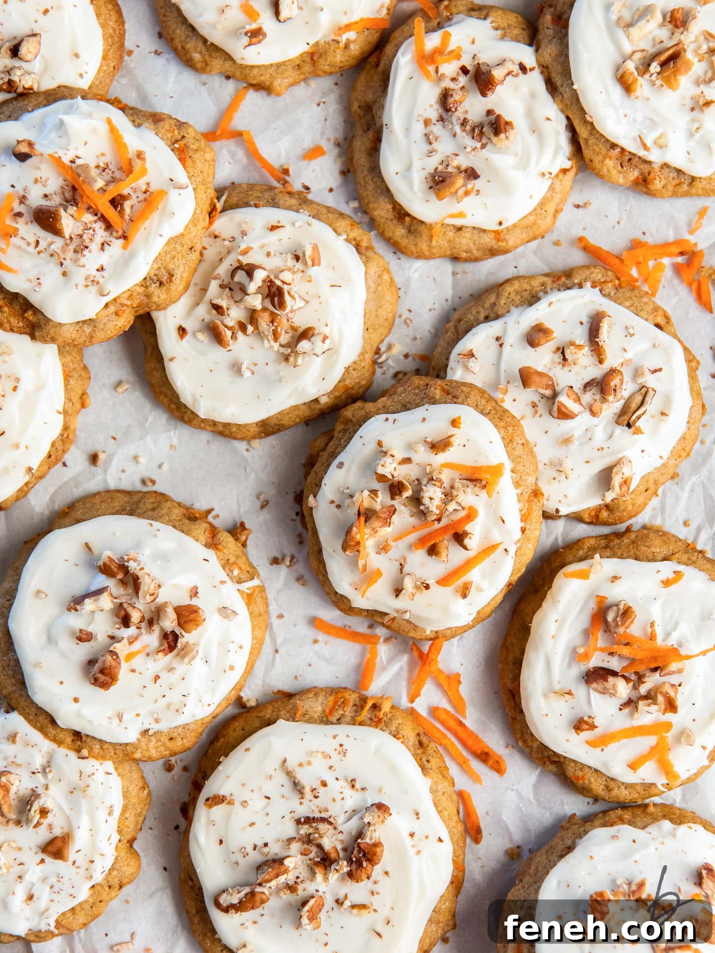 carrot cake cookies with cream cheese frosting garnished with chopped walnuts and carrot shreds.