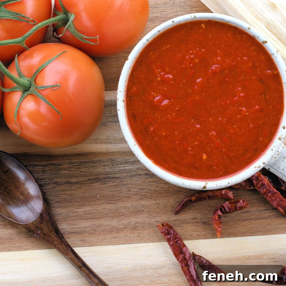 24bite: homemade red tamale sauce in a cup on a wooden surface with tomatoes and arbol chiles