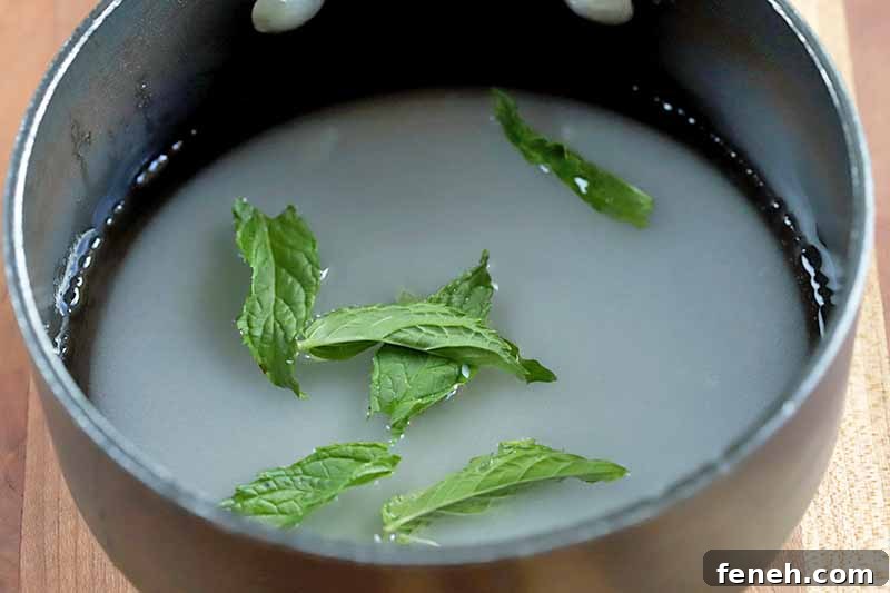 A nonstick saucepan of sugar, water, and mint leaves, on a brown wood surface.