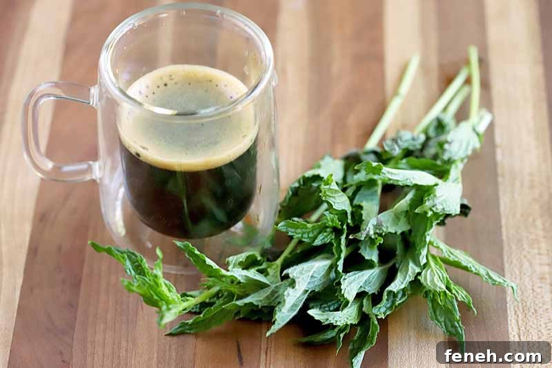 A glass mug of espresso and several sprigs of green fresh mint, on a wood surface.
