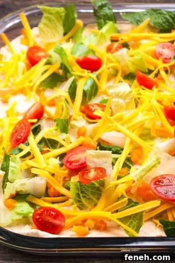 Layered gluten-free taco dip in a serving dish, showing layers of cream cheese, lettuce, peppers, onion, tomatoes, and shredded cheese.
