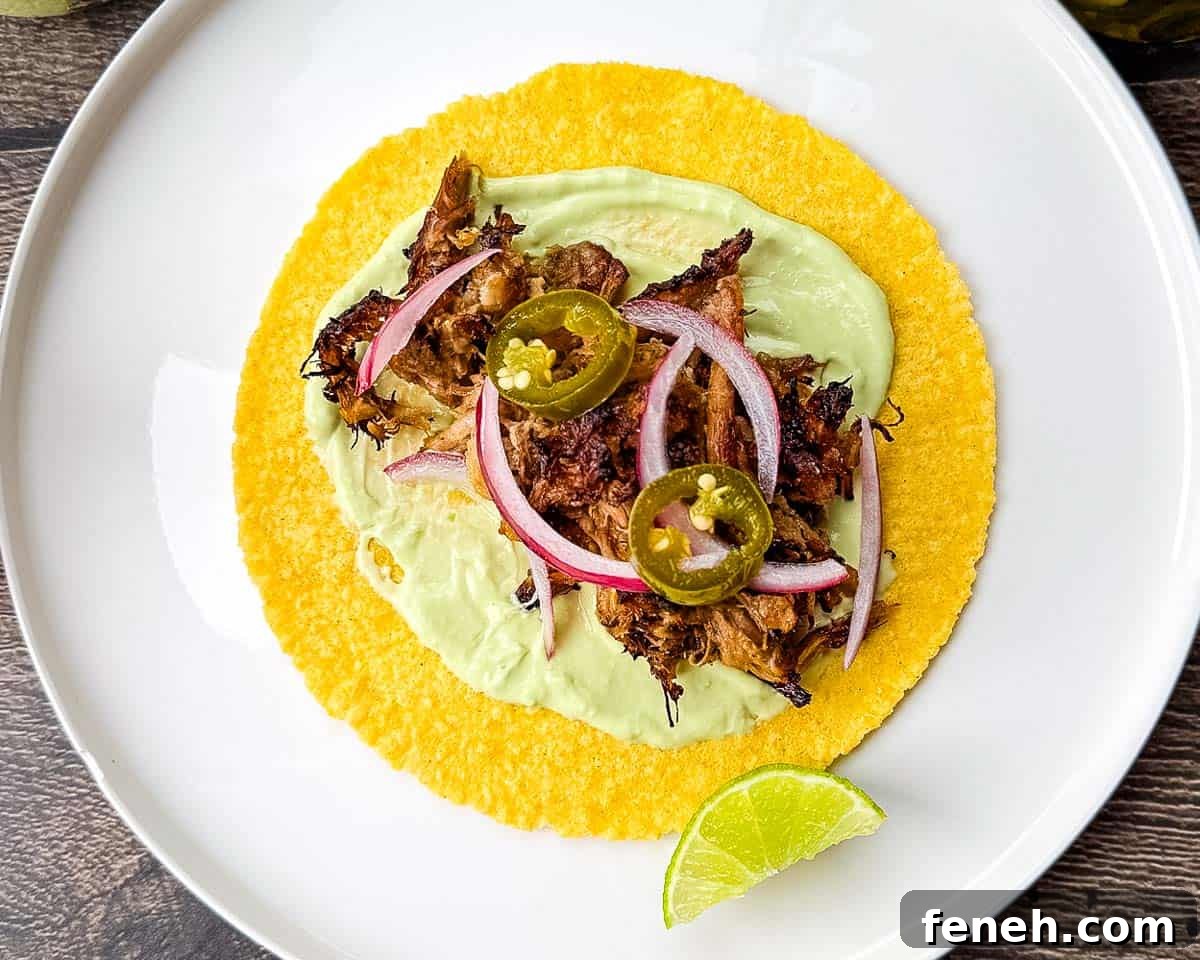 A corn tortilla topped with avocado crema, shredded crispy pork, pickled red onion, and pickled jalapeno.