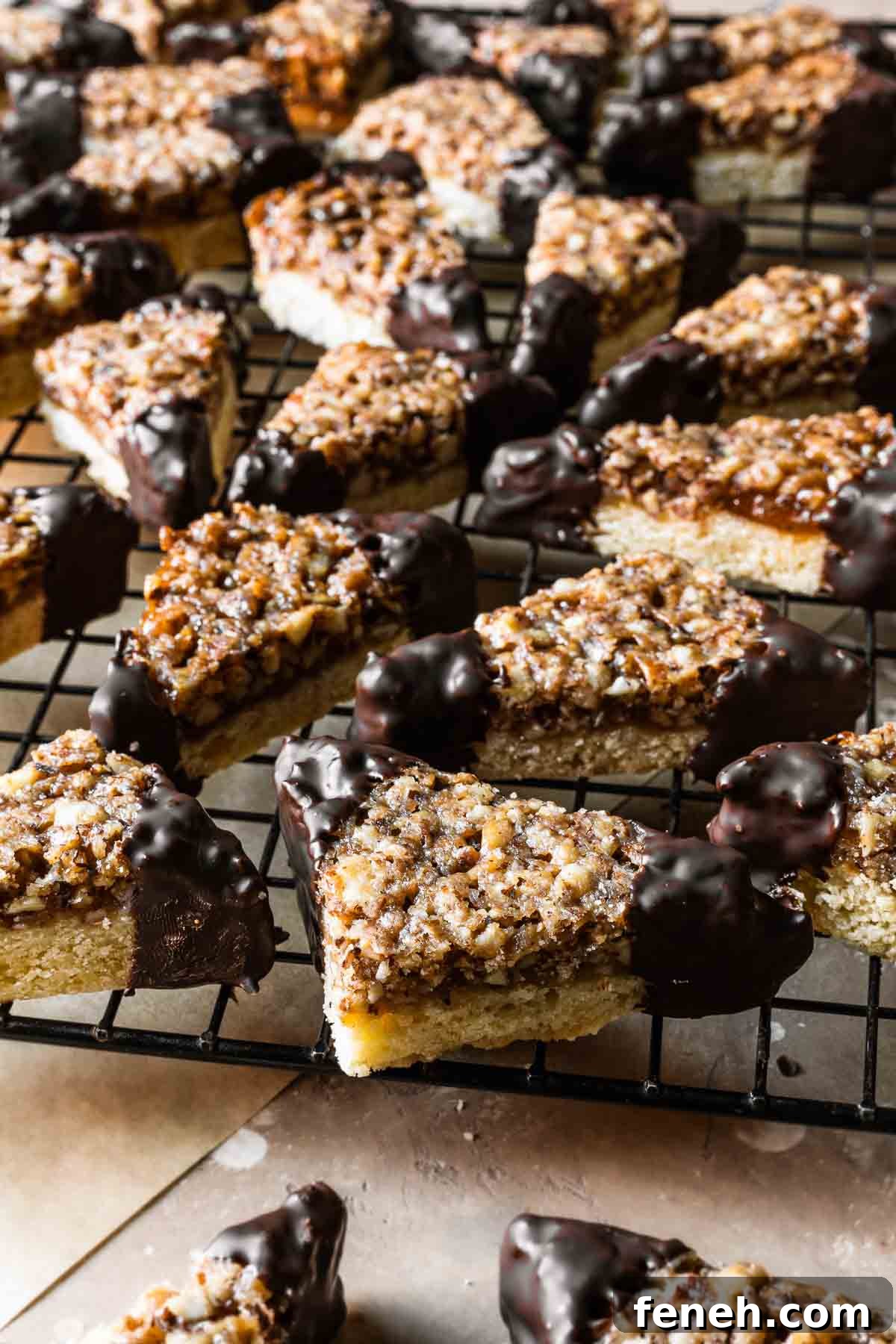 Triangular shortbread cookies with nut topping and chocolate dipped corners on a cookie rack.