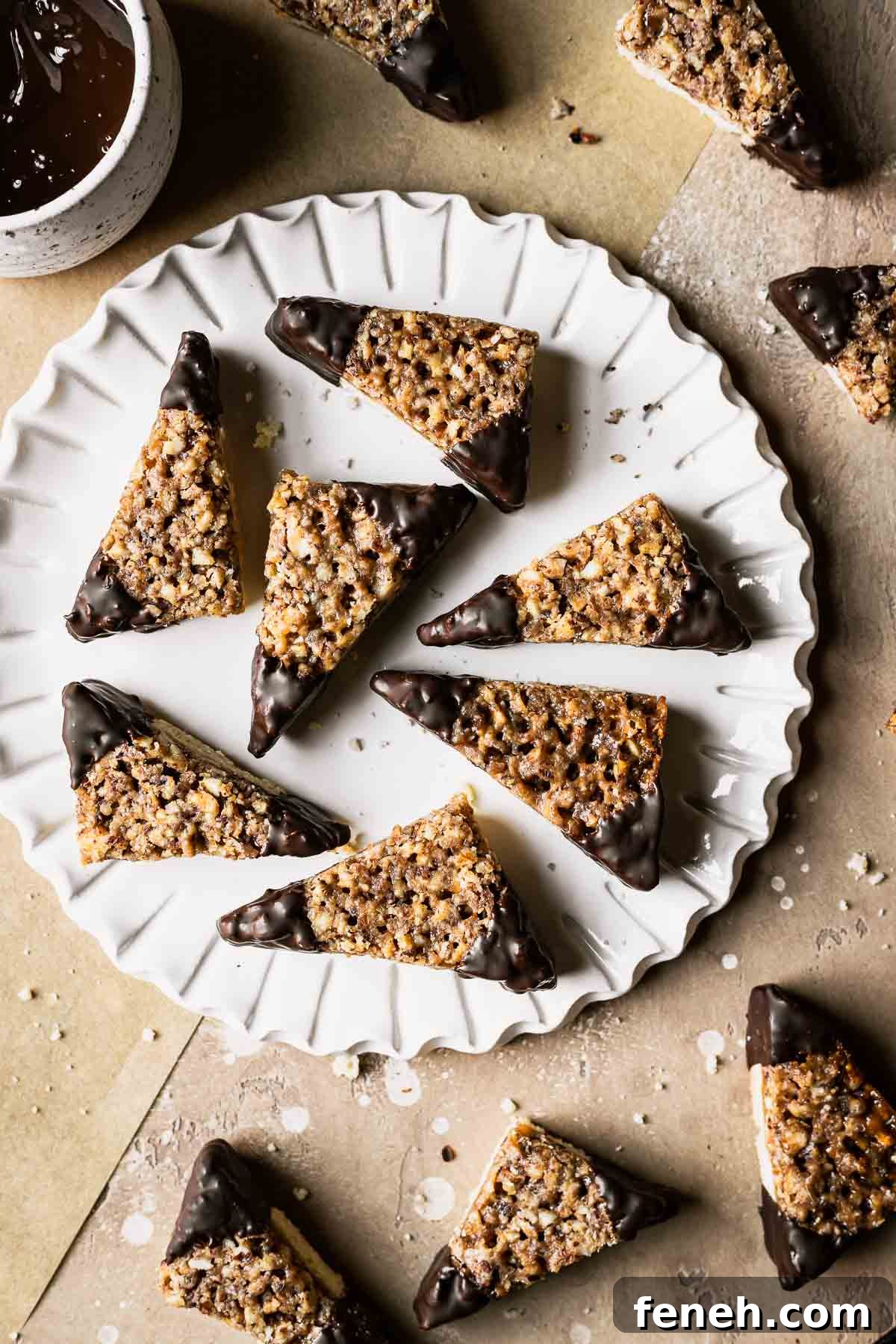 Triangle shaped nut cookies with corners dipped in chocolate on a white ceramic plate.