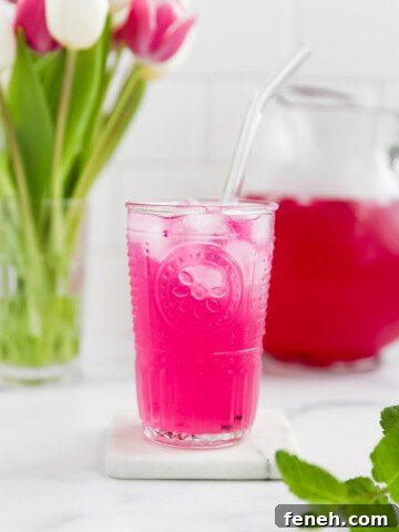 A glass of bright pink lemonade, filled with ice and a glass straw