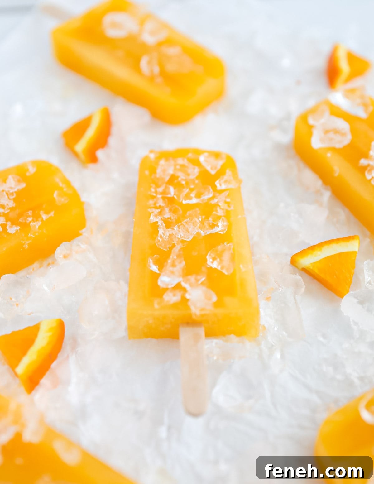A side angle picture of several orange ice pops, resting on a bed of crushed ice.