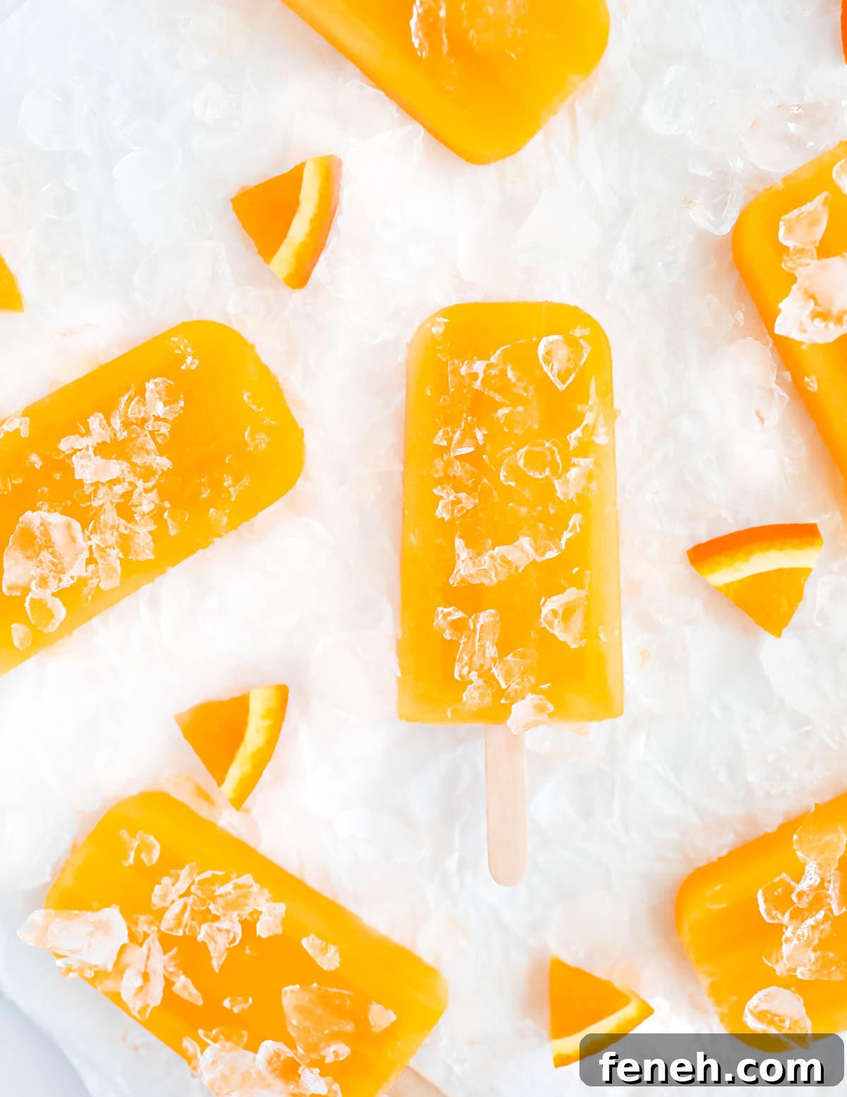 An overhead shot of 6 popsicles that are covered in clear crushed ice and surrounded by tiny orange slices