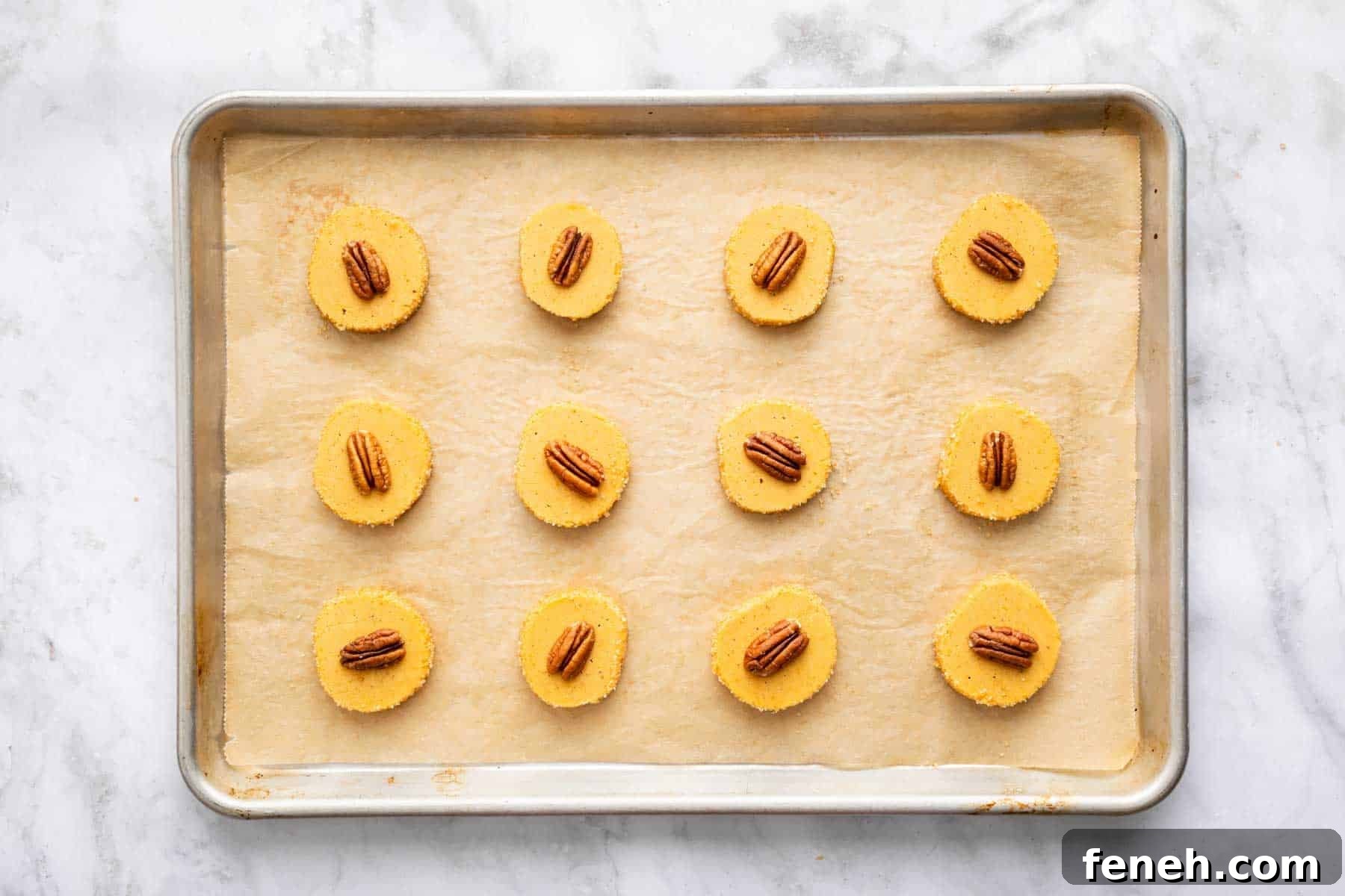 Twelve pumpkin shortbread cookies with a glazed pecan on top.