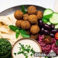 A falafel plate with crispy falafel balls, tahini falafel sauce, sumac onions, humus, zhoug and fresh vegetables.