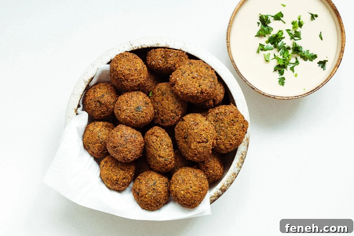 A ceramic bowl with crispy falafel balls and falafel patties next to a small bowl of falafel tahini sauce viewed from above.
